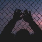 silhouette of persons hand on chain link fence