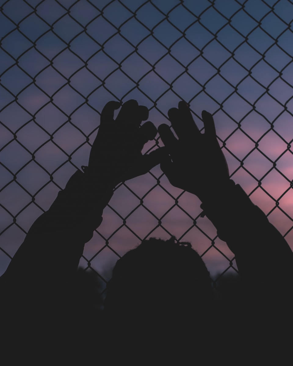 silhouette of persons hand on chain link fence