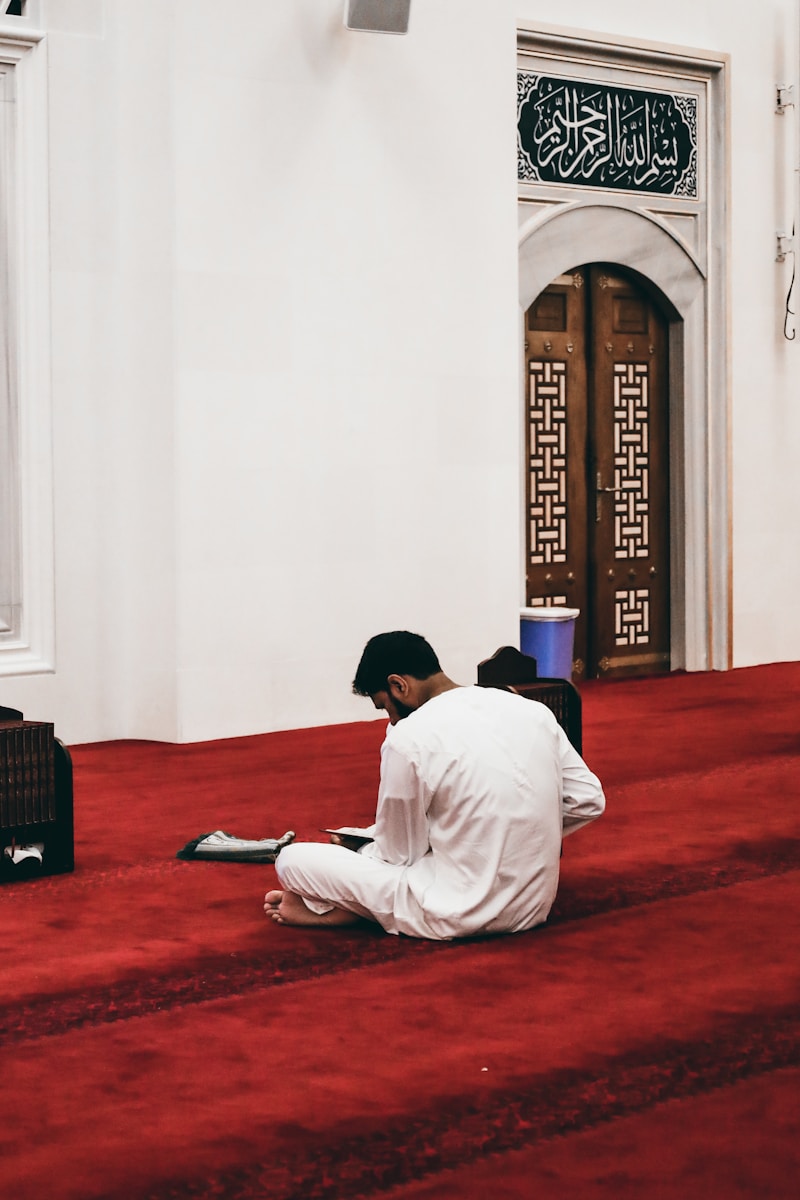 Photo by Ibrahim guetar a man sitting on the floor of a mosque reading a book