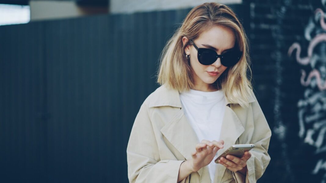 Woman in sunglasses using a smartphone outdoors