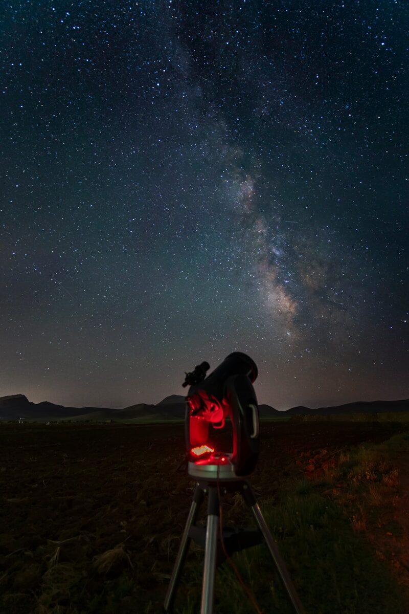 a telescope on a tripod in a field with the night sky in the background