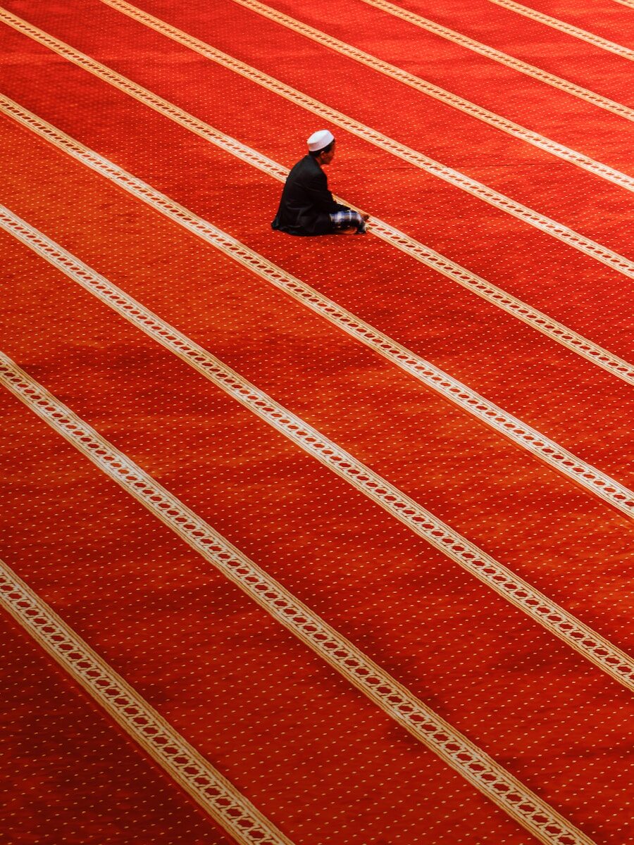 Man sitting on a patterned mosque carpet.