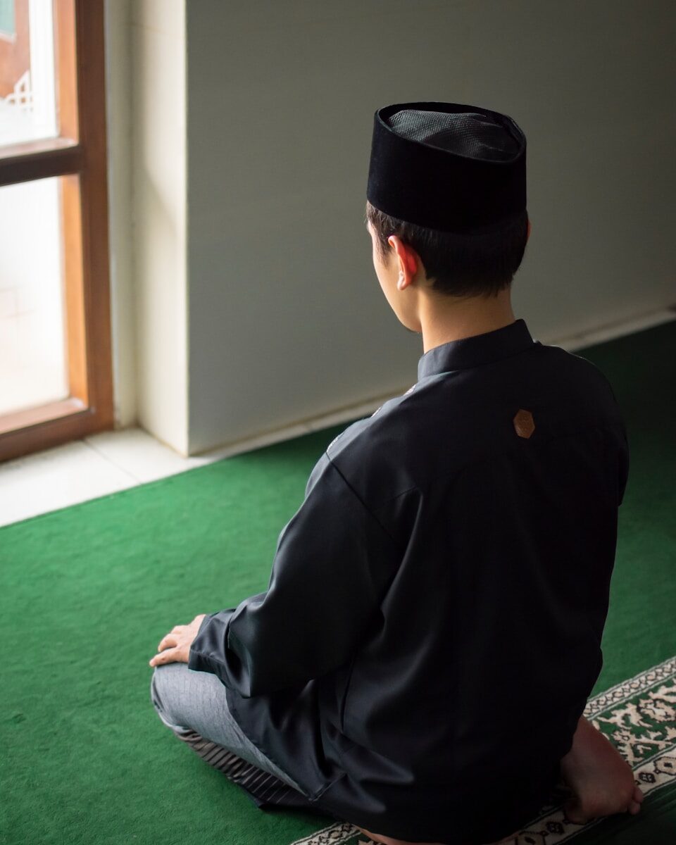 a man sitting on the floor wearing a black hat