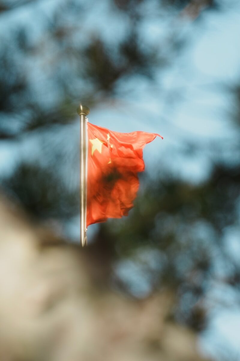 A chinese flag waves against a blurred background.
