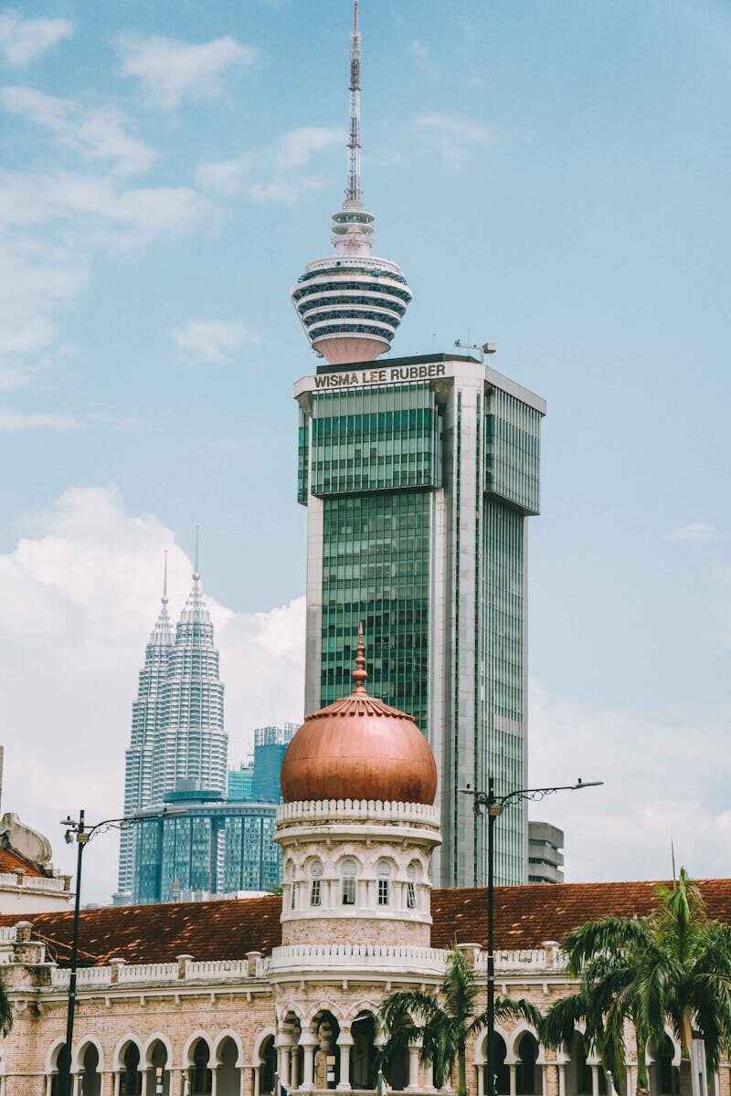 View of Kuala Lumpur skyline featuring the KL Tower and iconic Petronas Towers under a bright sky.