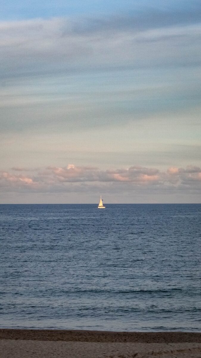 A lone sailboat on the ocean under a cloudy sky.
