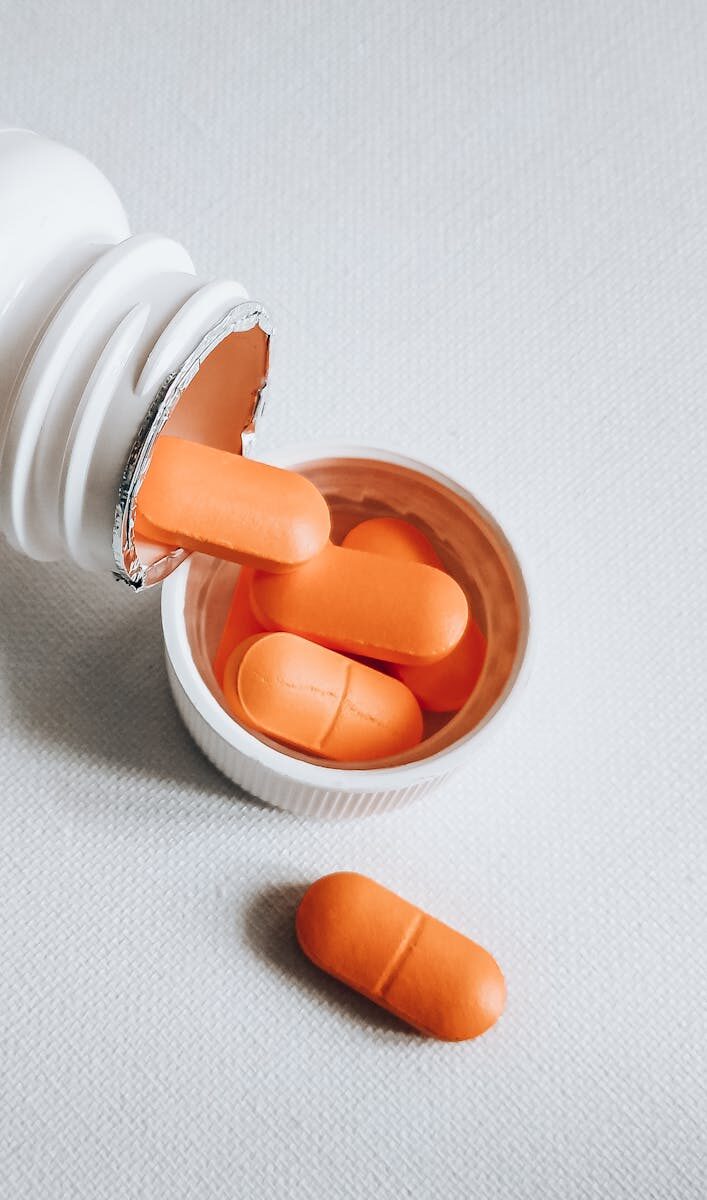 Close-up of orange pills spilling from a white bottle on a textured surface.