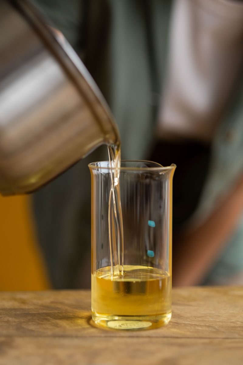 Detailed close-up of golden liquid candle wax being poured into a beaker in an artisan setting.
