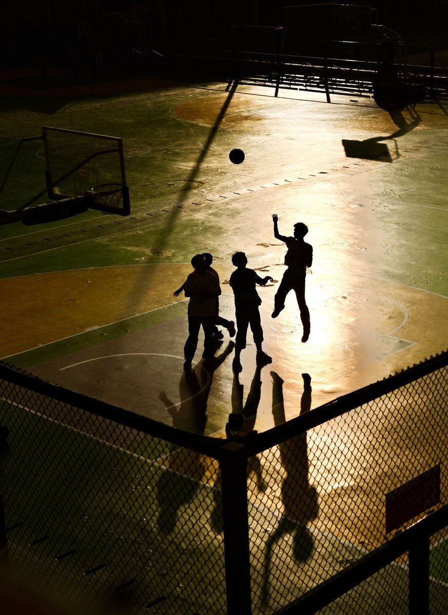 A dynamic silhouette of teens engaged in a lively basketball game at sunset on a court in Phuket, Thailand.