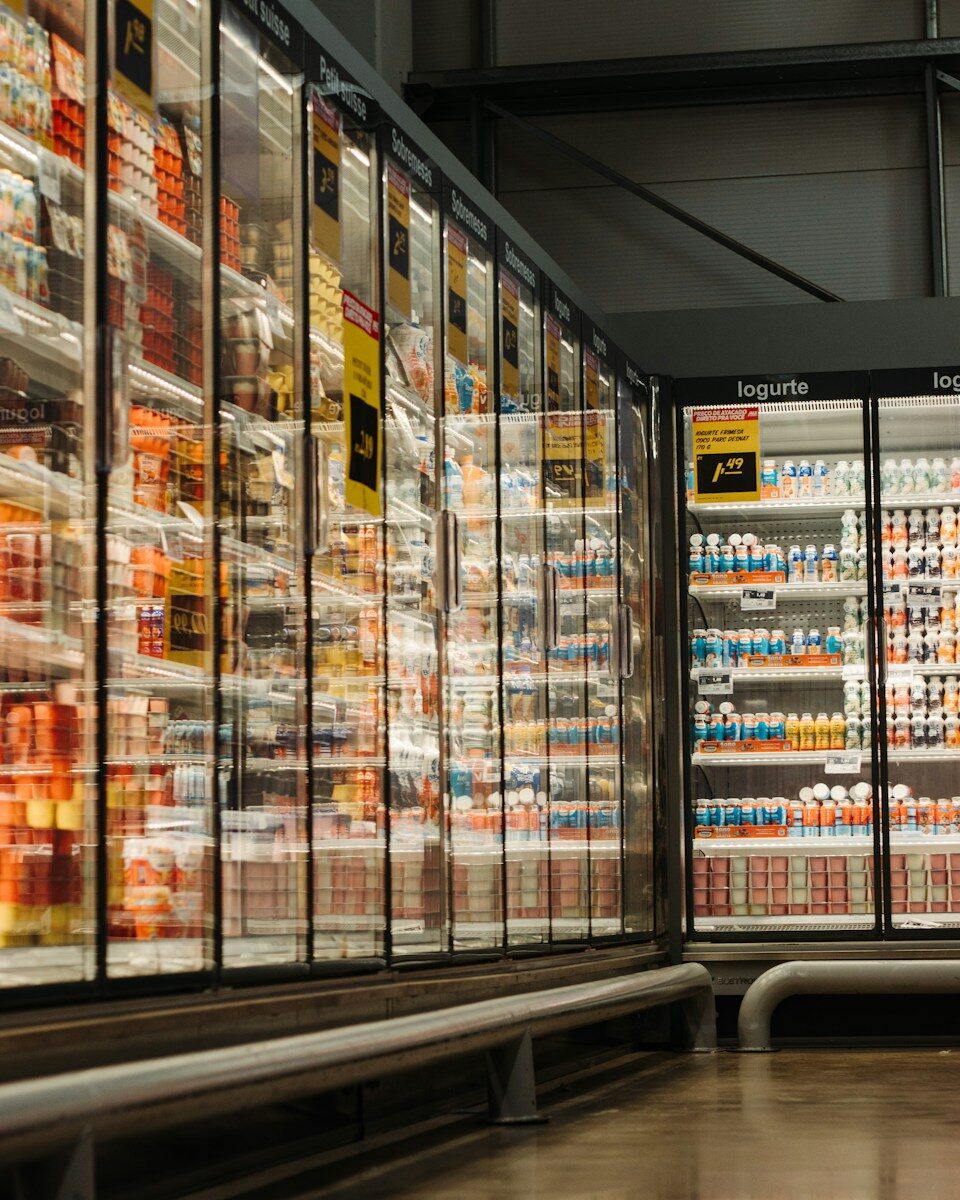 Glass refrigerated display cases filled with rows of yogurt in a grocery store