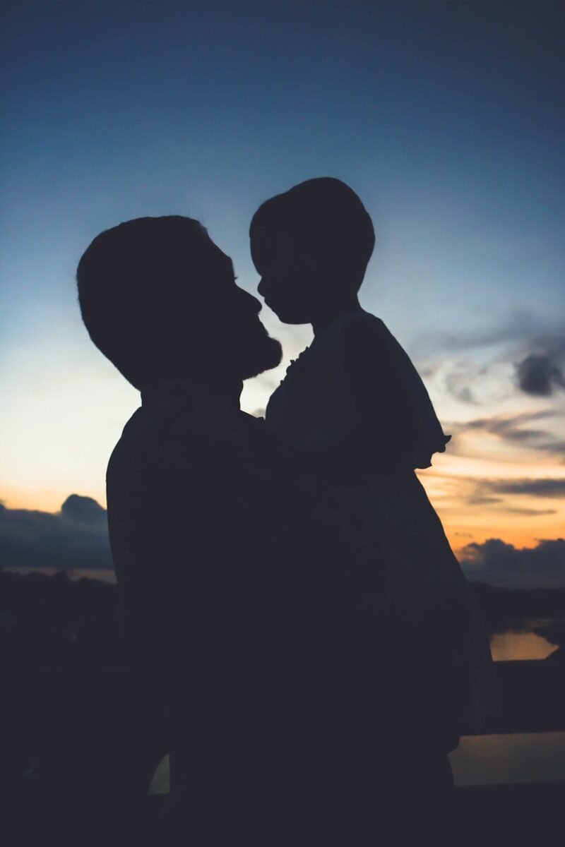 A silhouette of an adult holding a child against a warm orange sky